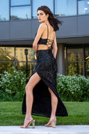 A woman in a black dress and heels poses confidently for a photo, showcasing her elegant style.