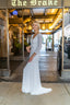 A beautiful bride poses elegantly in front of the Brake Hotel, showcasing her wedding dress and radiant smile.