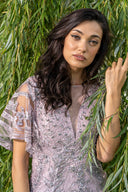 A woman wearing a dress is leaning against a tree, surrounded by greenery, exuding a sense of calm and tranquility.