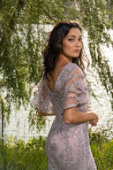 A woman in a flowing dress stands gracefully by a serene lake, surrounded by nature's beauty.