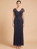 A woman modeling a floor-length navy blue evening gown with sheer cap sleeves, a V-neckline, and intricate beaded chevron patterns, set against a solid beige background.