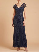 A woman modeling a floor-length navy blue evening gown with intricate beadwork and sequin patterns, set against a solid beige studio background.