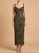 A woman modeling a sleeveless, midi-length olive green gown with intricate beadwork and sequin embellishments against a solid beige studio background.
