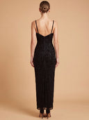 A woman shown from the back wearing a black beaded spaghetti-strap maxi dress against a solid beige studio background.