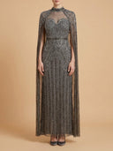 A model wearing a floor-length gray lace gown with a high neck, sheer mesh overlay, and a matching sheer cape, standing against a solid beige background.