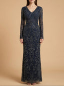 A woman modeling a long-sleeve, floor-length navy lace gown with intricate beadwork and sequins against a solid beige studio background.
