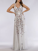 A woman poses with hands on hips in the Lara 29544—an elegant sleeveless white beaded dress with a V-neckline, open cross back, and flowy skirt—set against a plain light background, perfect for a unique wedding look.