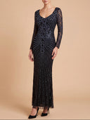 A woman modeling a floor-length black lace and sequin evening gown with long sleeves and a V-neckline, standing against a solid beige studio background.