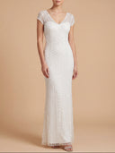 A woman modeling a floor-length white gown with cap sleeves, a V-neckline, and intricate beaded chevron detailing, set against a solid beige studio background.