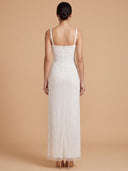 A woman viewed from the back wearing a sleeveless white maxi dress with thin straps, a fitted bodice, and a long textured skirt, standing against a warm beige studio background.