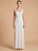 A woman modeling a sleeveless, floor-length white gown with thin straps, a sweetheart neckline, and intricate floral lace and bead embellishments, set against a solid beige studio background.