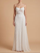 A woman modeling a floor-length white gown with a fitted corset-style bodice, sheer overlay panels, and a flowing tulle skirt against a warm beige studio background.