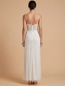 A woman shown from the back wearing a sleeveless white lace maxi dress with thin straps, a sheer structured back, and a fitted flared skirt, standing against a warm beige studio background.