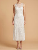 A woman modeling a sleeveless white lace midi dress with a sheer illusion neckline, fitted waist, and flared skirt, standing against a warm beige studio background.