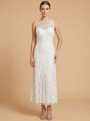 A woman modeling a sleeveless white lace midi dress with a sheer high neckline and floral applique, standing against a solid beige studio background.