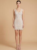 A woman models a sleeveless, bodycon mini dress covered in intricate floral lace and bead embroidery. The dress features a deep V-neckline and is shown against a solid, warm beige studio backdrop.