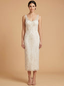 A woman modeling a sleeveless ivory lace midi dress with a V-neckline, photographed against a solid warm beige studio background.
