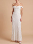 An off-the-shoulder floor-length white gown with a fitted bodice and pleated skirt, shown on a model against a warm beige studio background.