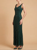 A woman modeling a sleeveless, floor-length dark green sequined gown with a V-neckline and pleated skirt, standing against a solid beige studio background.